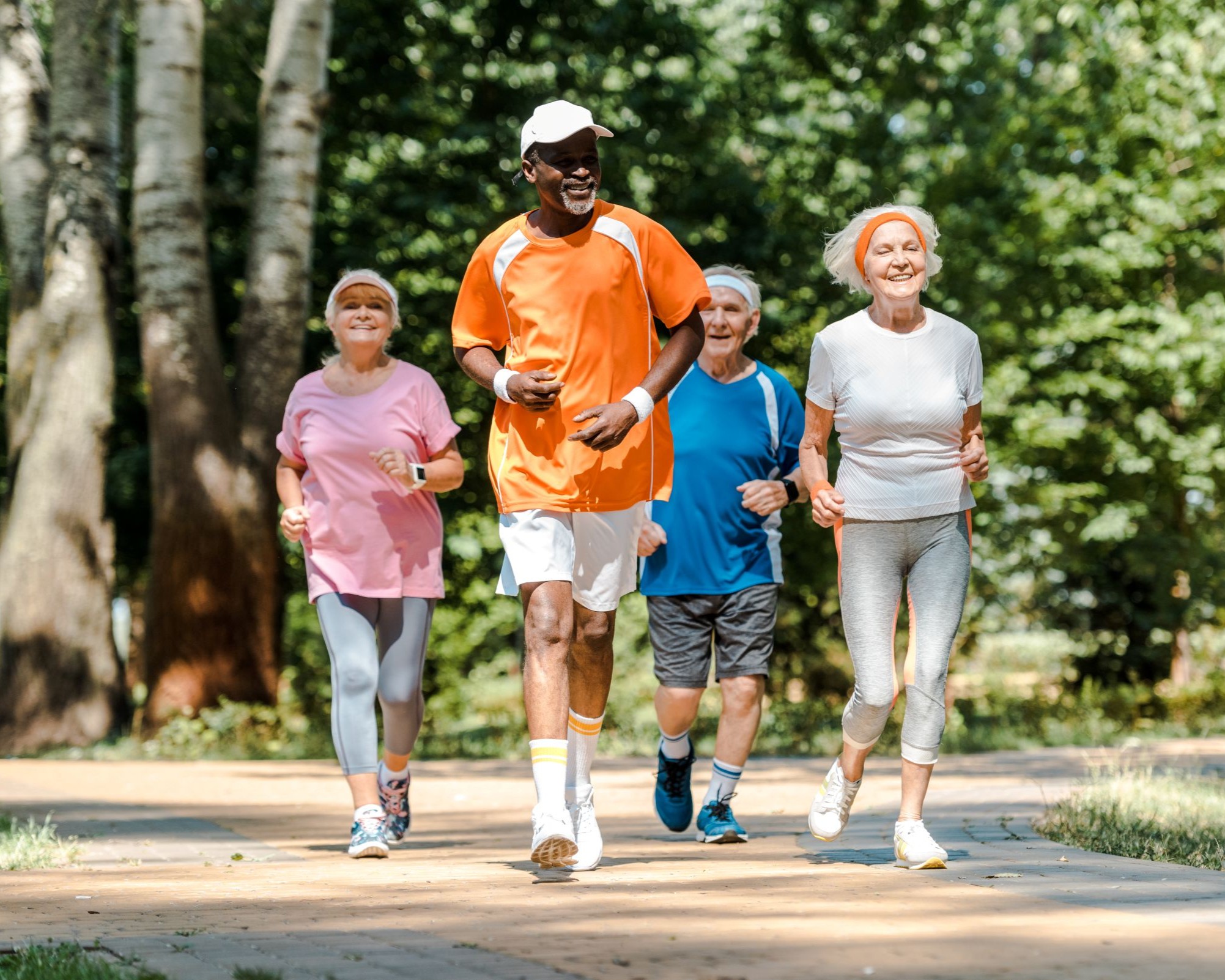 An older Black man and three older women jog together outdoors on a sunny day.