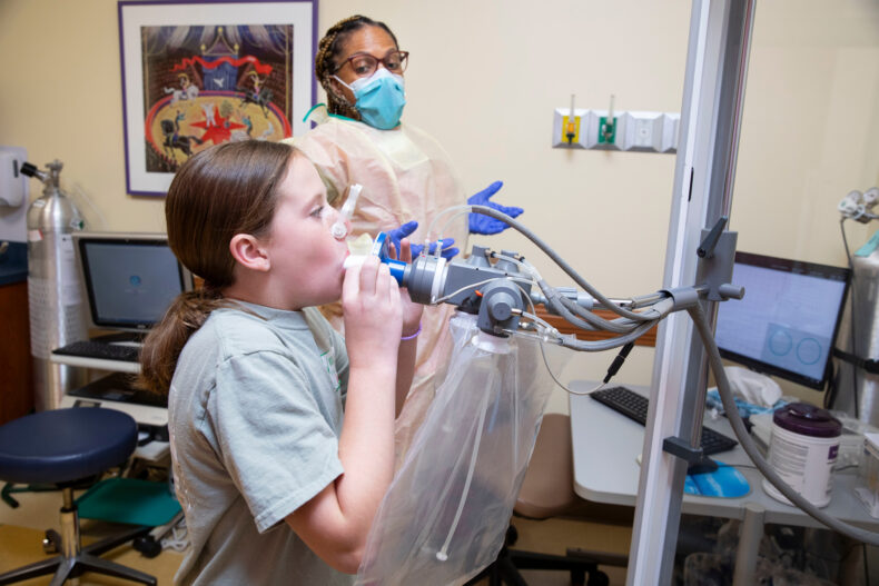Registered respiratory therapist Natasha Vanderbilt, RRT, encourages 10-year-old Kate to exhale a complete breath during a lung function test in the Pediatric Pulmonary Medicine clinic. 