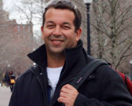 Dr. Marcelo Cordeiro-Santos outside in a park with a backpack over one shoulder.