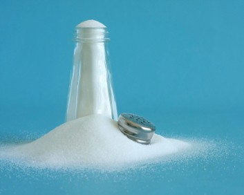 An overflowing salt shaker against a turquoise blue background