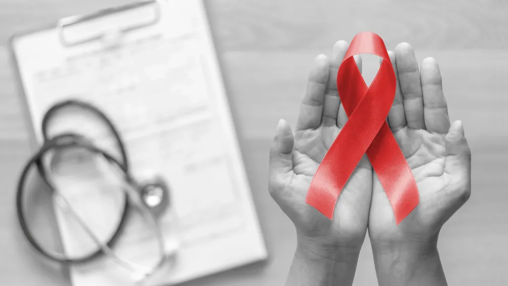 A black and white image of hands and a medical chart and stethescope with a red AIDS ribbon.