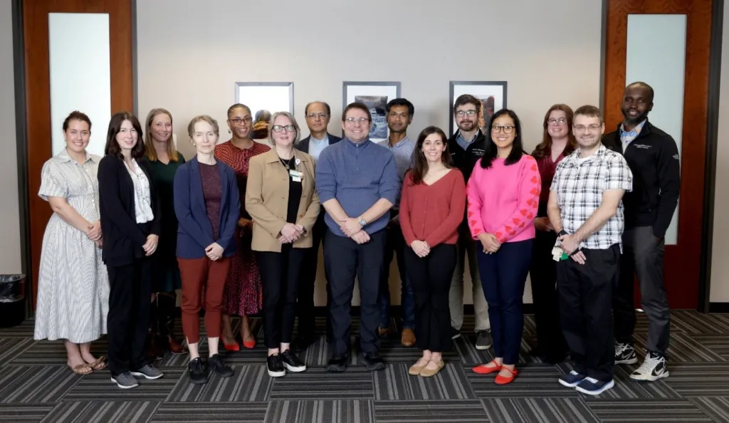 About 15 researchers and support staff pose in an academic hallway.